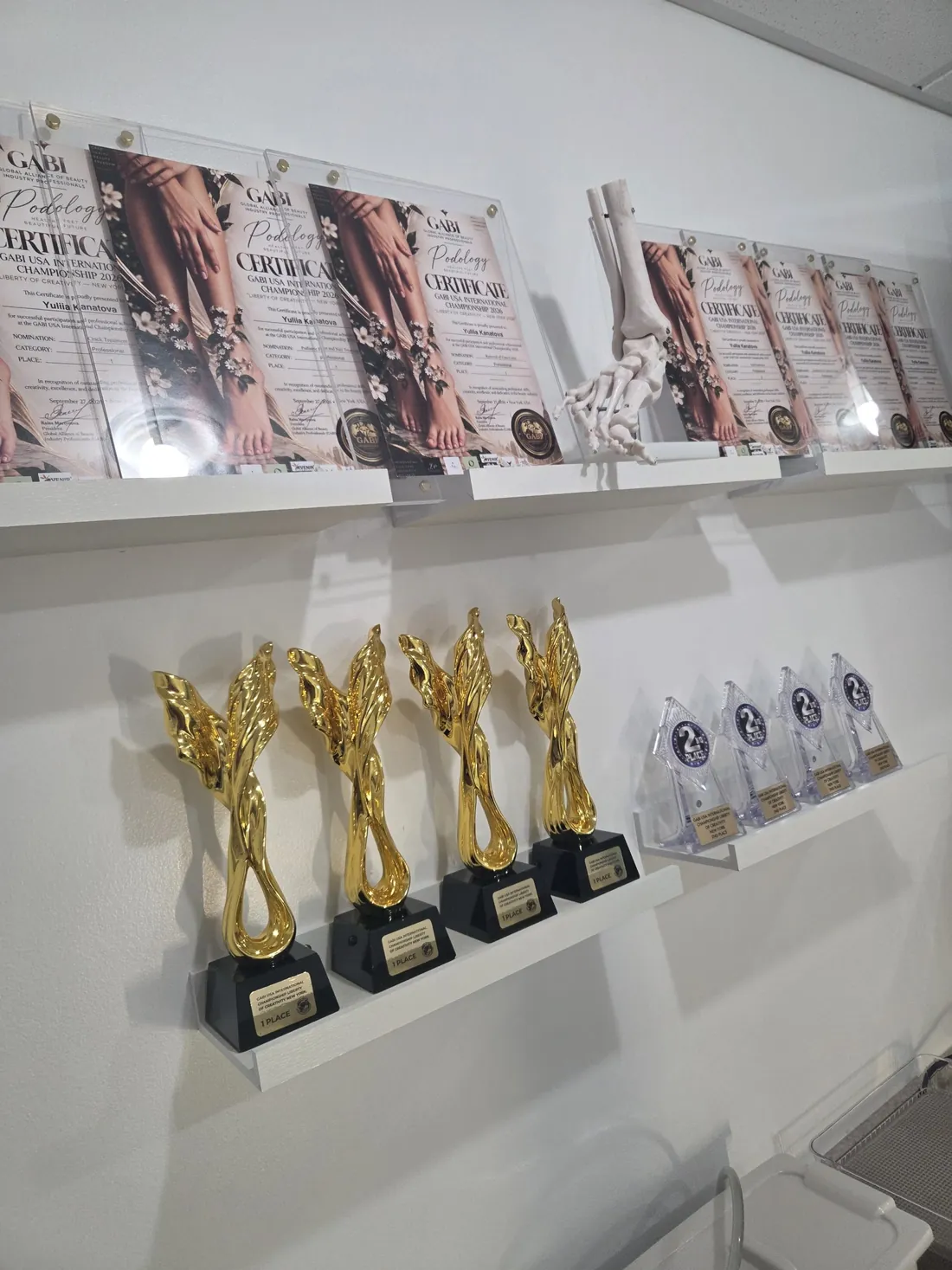 Award wall at MediPedi in Troy, MI with GABI certificates, trophies and a foot skeleton model